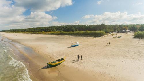 a group of people standing on a beach with a boat at Flatbook Rodzinne Apartamenty Jantar Resort z Parkingiem, Placem Zabaw i Wiatą Grillową in Jantar