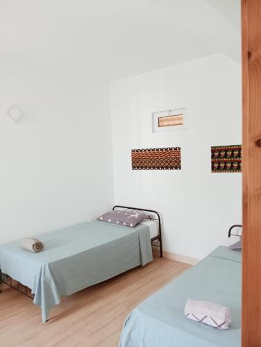 two beds in a room with white walls and wooden floors at Appart Chris Mindelo in Mindelo
