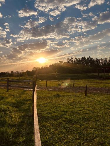 a fence in a field with the sunset in the background at Cabana de teto de vidro in Santa Cruz do Sul