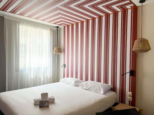 a bedroom with a white bed with a red and white striped wall at ibis Styles Nimes Gare Centre in Nîmes