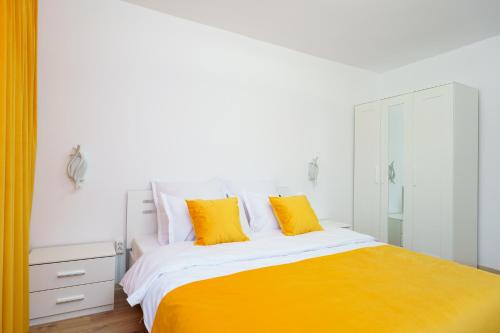a white bedroom with a bed with orange and white pillows at Joy Apartament in Nehoiu