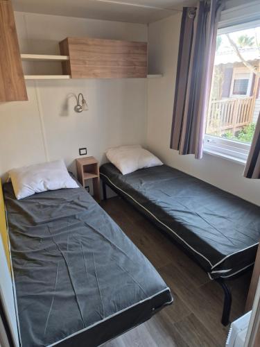 two beds in a small room with a window at Mobilhome, Camping Le Marisol in Torreilles