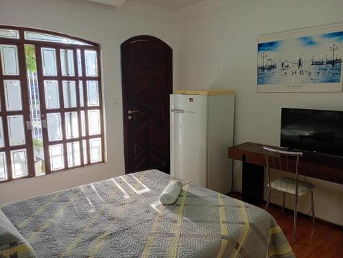a bedroom with a bed and a desk and a refrigerator at Pousada Fernanda in Guarapuava
