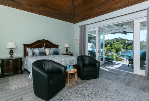 a bedroom with a bed and two chairs and a balcony at Mahalo Villa Beachfront Generator in Cruz Bay