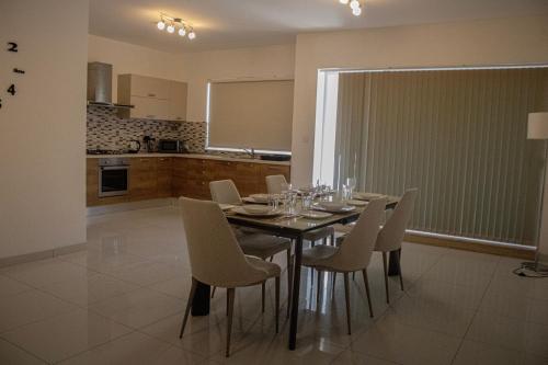 a dining room table with white chairs and a kitchen at Modern 3 bedroom with AC apartment in Żabbar