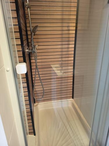 a shower in a bathroom with a wooden wall at Appartement du Fournil in Bréal-sous-Montfort