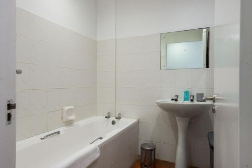 a white bathroom with a tub and a sink at Rustic Beachfront Apt! Shared Pool! in Umdloti