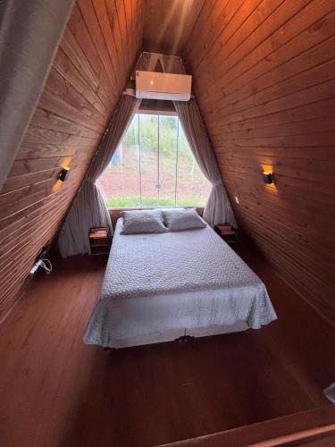 a bed in a wooden room with a window at Amorência Chalé Luz da lua in Campo Largo