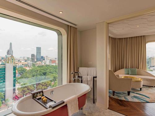 a bathroom with a bath tub and a bedroom at Hotel Des Arts Saigon Mgallery Collection in Ho Chi Minh City