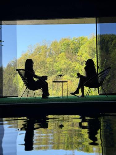 two women sitting in chairs looking out of a window at Vikendica Tuzla baracuda bazen in Slavinovići