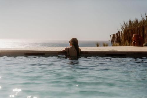a woman is sitting in a swimming pool at oceanHUTS Coxos Adults Only from age 14 in Ericeira