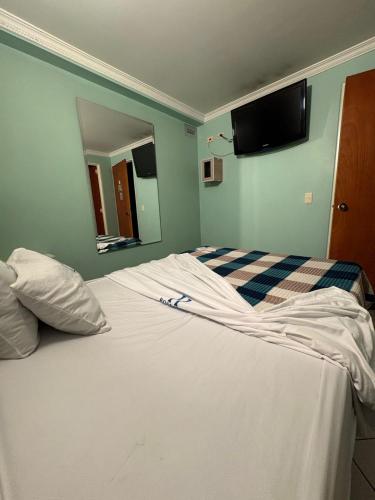 a bedroom with a white bed with a tv on the wall at Hotel Romanza in Bogotá