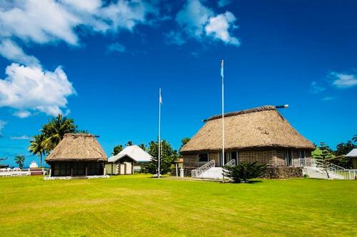two buildings with straw roofs on a green field at Vunakavika House - Village Stay in Nadi