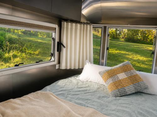 a bed in an rv with two windows at One Life Glamping Caravan Rawson in Rawson