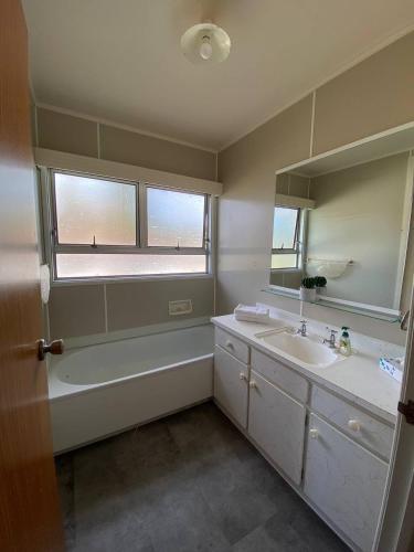 a bathroom with a tub and a sink and a mirror at Waitangi Beach House in Paihia
