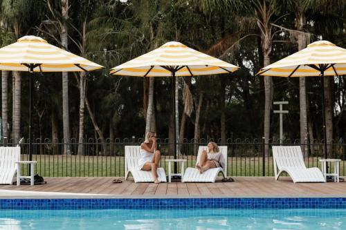 two women sitting in chairs next to a pool with umbrellas at Tasman Holiday Parks - Kioloa Beach in Kioloa
