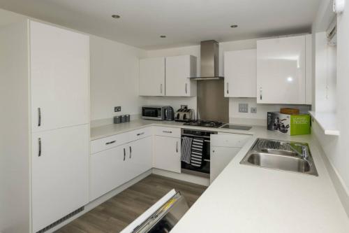 a white kitchen with white cabinets and a sink at Cosy 5 Bedroom House With Parking in Chatham