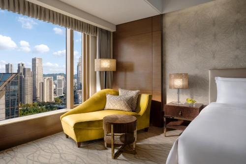 a hotel room with a bed and a yellow chair and a window at Kempinski Hotel Chongqing in Chongqing