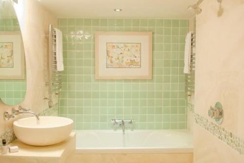 Baño de azulejos verdes con lavabo y bañera en Swan House, en Beccles