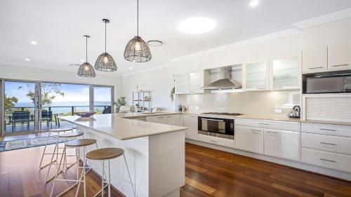 a kitchen with white cabinets and a island with bar stools at 'Gone Coastal' by HolidayCo in Killcare