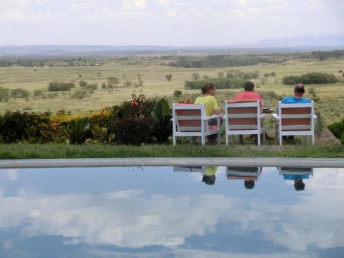 three people sitting on chairs near a pool of water at Mwanzo Lodge in Naivasha