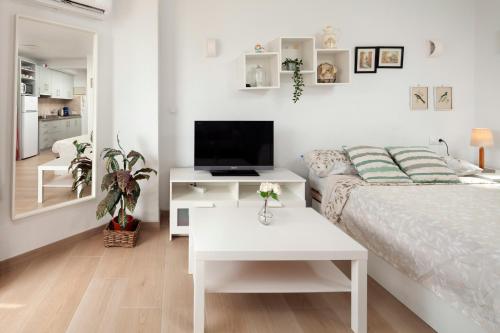a white bedroom with a bed and a tv at Sol y breeze in Torre del Mar