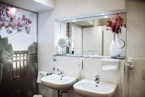 a bathroom with two sinks and a mirror and a vase with flowers at Hotel Prinzregent in Nuremberg