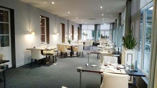 a dining room with tables and chairs and windows at Logis Au Grand Hotel in Mayenne