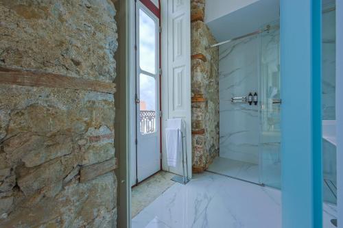 a bathroom with a walk in shower next to a stone wall at Casa da Portagem by PURUS in Coimbra