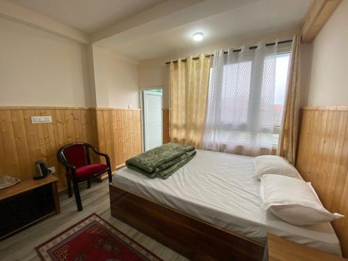 a bedroom with a bed and a chair and a window at Tenzin's Inn in Jālāpahār