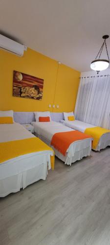 three beds in a room with yellow and orange at Pousada Buona Serata in Bento Gonçalves