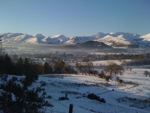 a snowy field with snow covered mountains in the background at Woodside B&B in Keswick