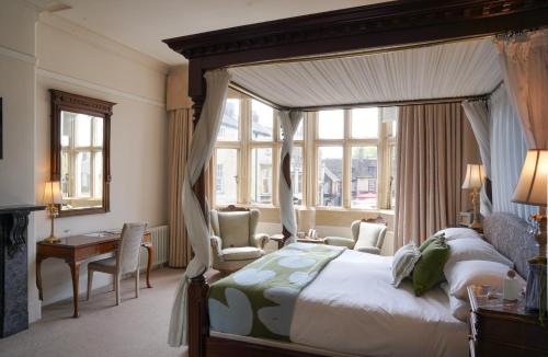 a bedroom with a canopy bed with a desk and chairs at The Falcon Hotel in Uppingham