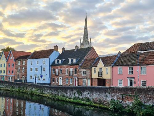a row of houses next to a river with a church at Elm Barn Lodge in Freethorpe