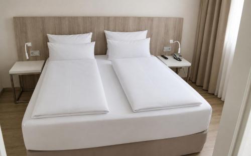 a large white bed with white sheets and pillows at DORMERO Hotel Fürth in Fürth