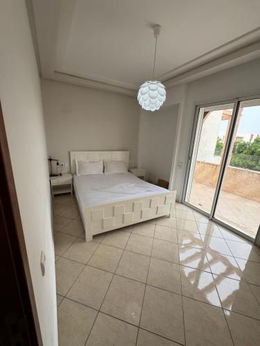 a white bedroom with a bed and a large window at Cozy Seaside Villa in Bir Jedíd Saint-Hubert