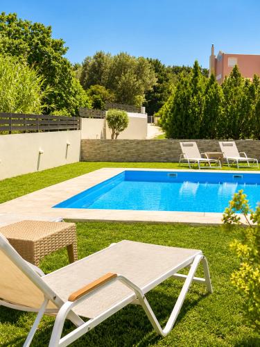 a swimming pool with two lawn chairs and a table at Villa Rose Ground Floor - Private Swimming Pool Garden in Koskinou