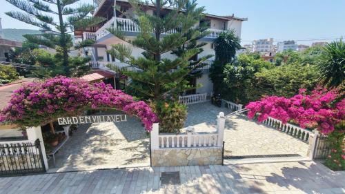 a white fence with pink flowers in front of a building at Garden Villa Veli in Ksamil