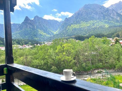 a coffee cup sitting on a window sill with a view of mountains at Mountain Stream Serenity - AC and Free Parking in Buşteni