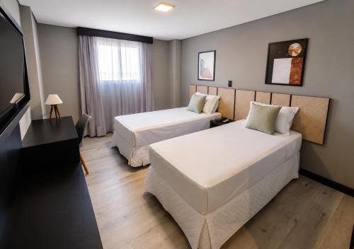 a hotel room with two beds and a flat screen tv at Tulip Inn Bauru in Bauru