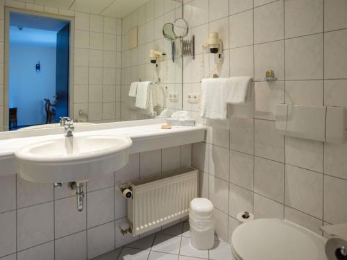 a white bathroom with a sink and a toilet at Mercure Hotel Plaza Magdeburg in Magdeburg