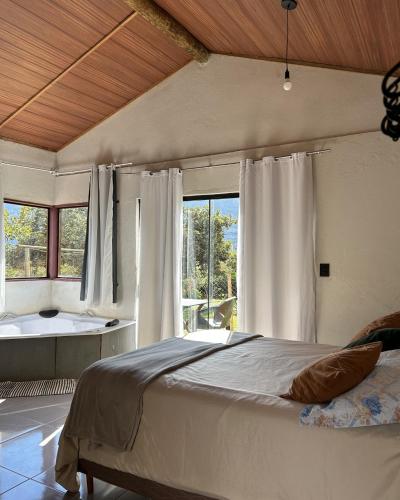 a bedroom with a bed and a tub and windows at Chalé Lumiar in Santana do Riacho