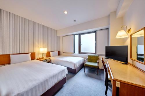 a hotel room with two beds and a desk and a tv at Smile Hotel Nihombashi Mitsukoshimae in Tokyo