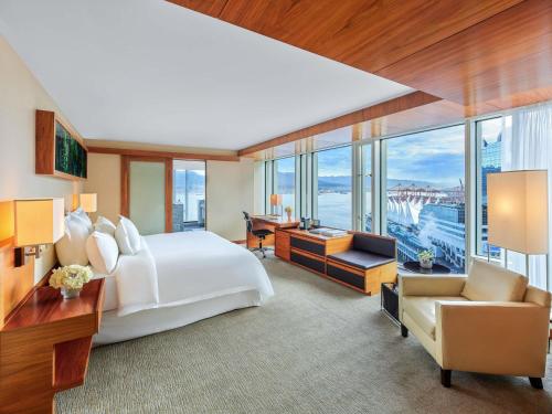 a bedroom with a large white bed and a desk and chair at Fairmont Pacific Rim in Vancouver
