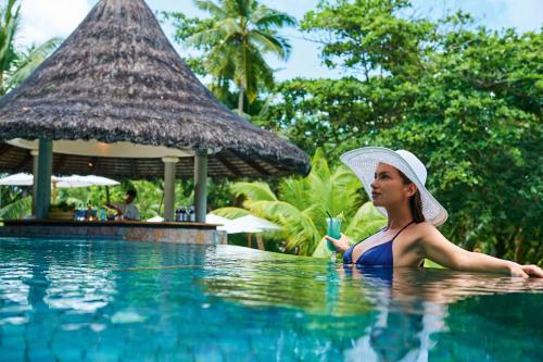 a woman in a hat sitting in a swimming pool at Constance Lemuria in Grand'Anse Praslin