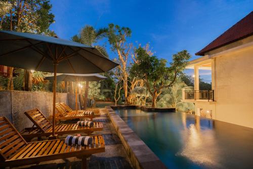 a swimming pool with two chairs and an umbrella at Kamasan Nusa Penida By Reccoma in Nusa Penida