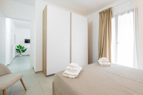 a white bedroom with towels on a bed and a chair at Sa concia in Teulada