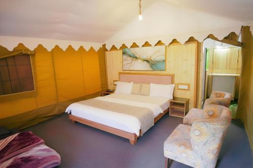 a bedroom with a large bed and a chair at Palki Camps and Resorts in Kailāna