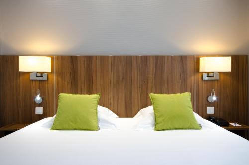 a large white bed with two green pillows at Best Western Plus Hotel Plaisance in Villefranche-sur-Saône