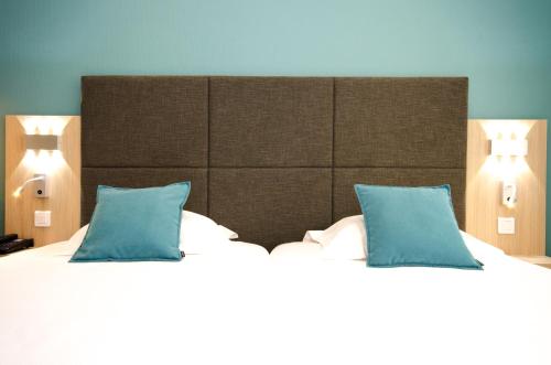 a bedroom with a large bed with two blue pillows at Best Western Plus Hotel Plaisance in Villefranche-sur-Saône